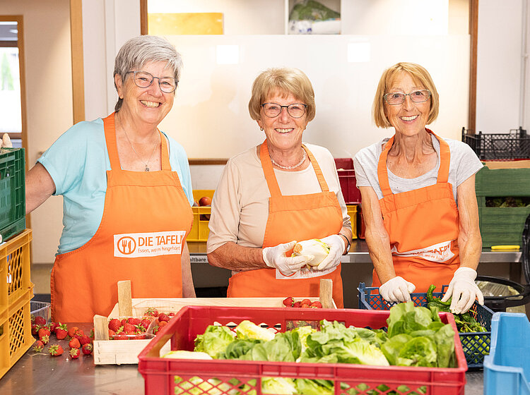 Freiwillige bei der Arbeit Drei Freiwillige der Tettnanger Tafel lächeln, während sie frisches Gemüse sortieren